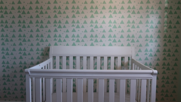 A baby cot next to a wall with a white and green wallpaper.